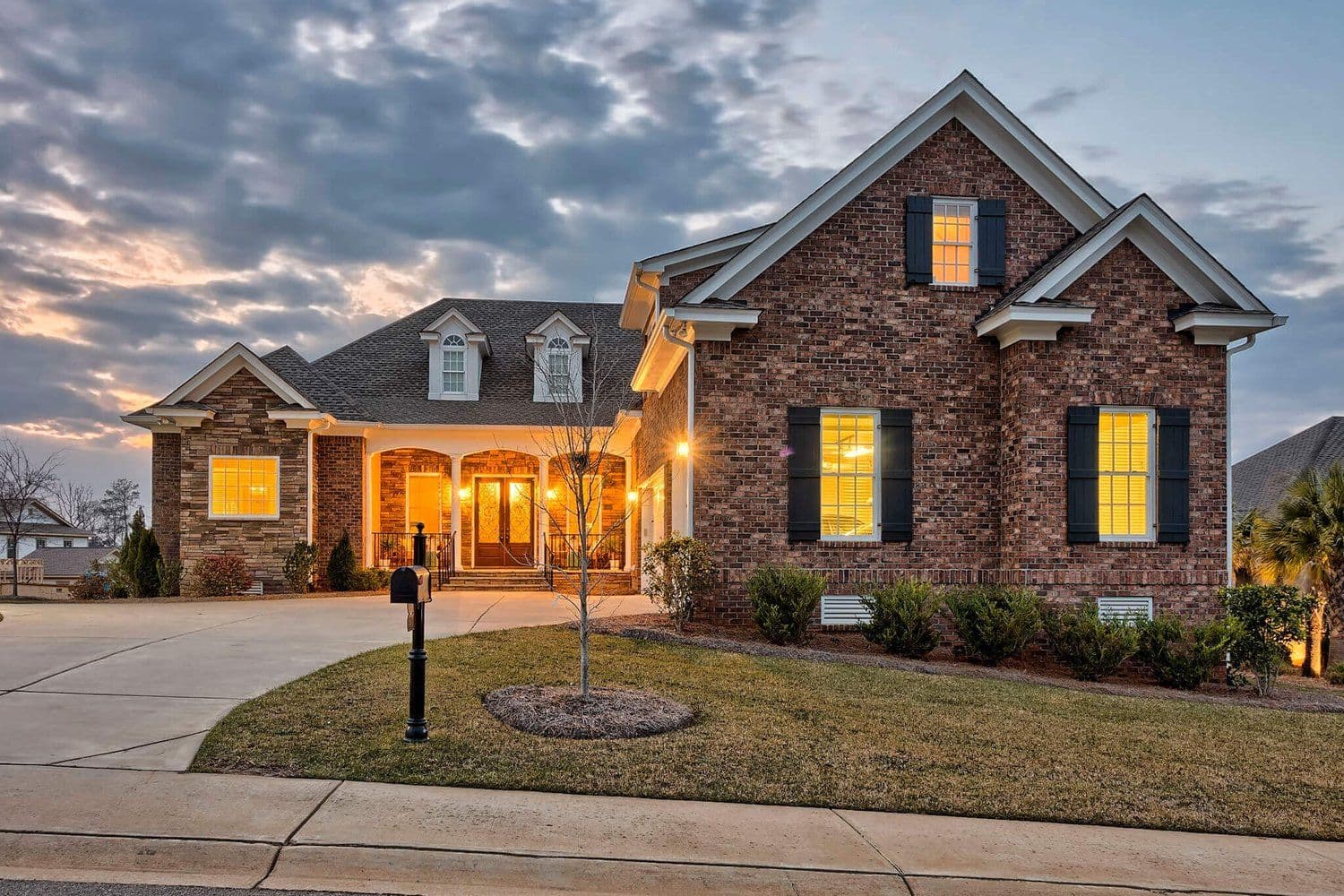 Brick home at dusk with lights glowing in the windows and porch