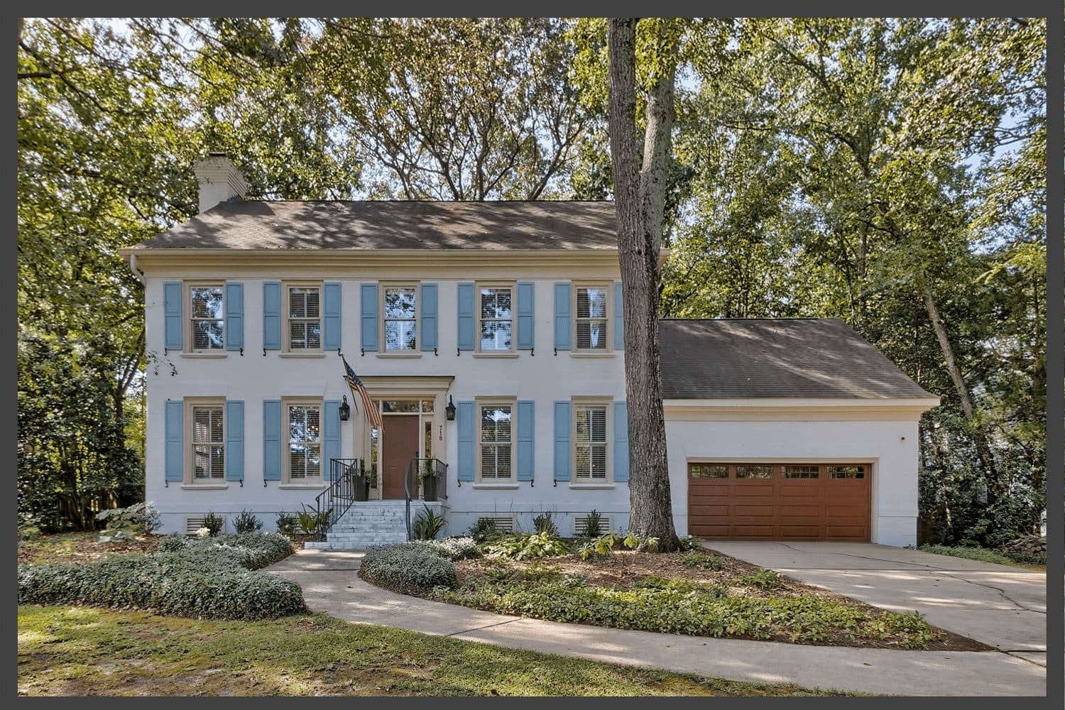 Two-story white home with light blue shutters among mature trees