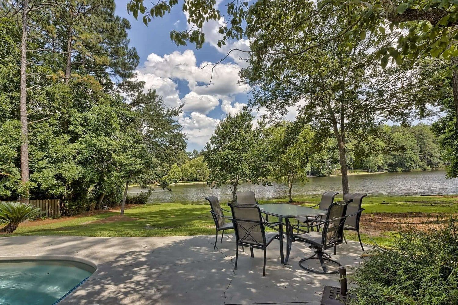 Stone patio with a dining set overlooking the lake through trees