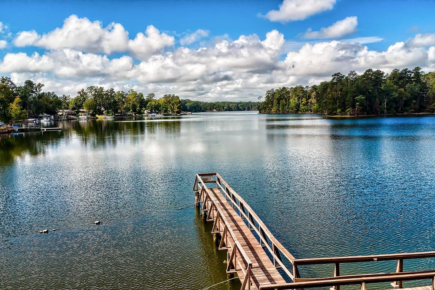 Wooden pier extending into a calm lake under a bright blue sky