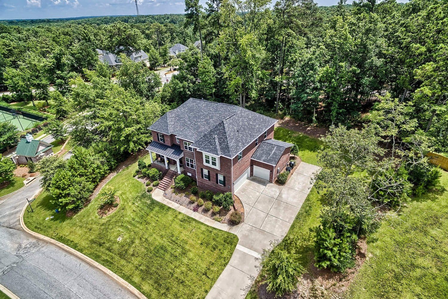Aerial of a brick home with a grey roof on a wooded lot