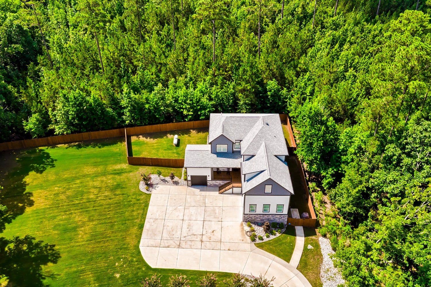 Aerial of a gray and white two-story house with a wide driveway on a wooded lot