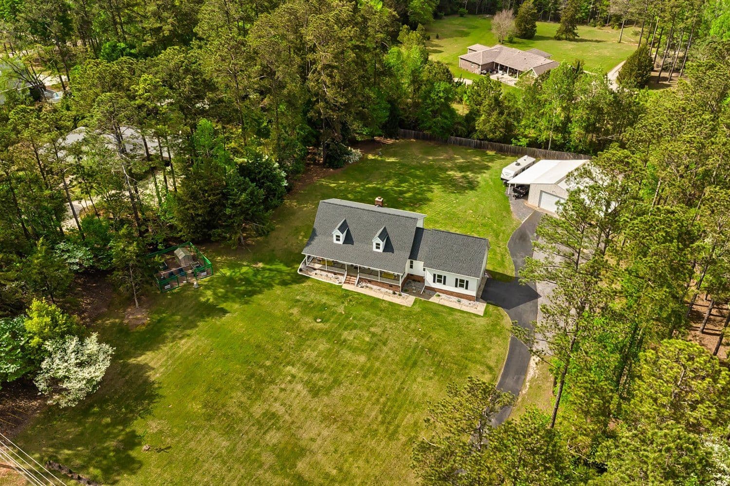 Aerial of a light-colored two-story home with a screened porch on a large lawn among pine trees