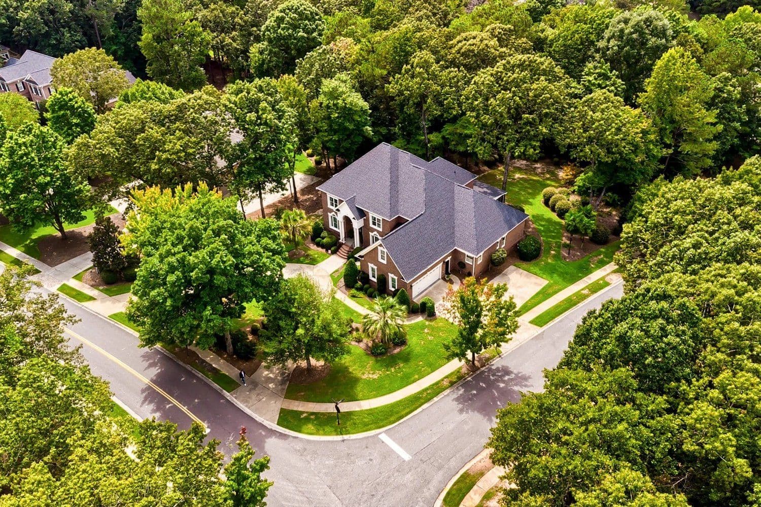 Aerial of a large dark-shingled house among trees beside a curved street