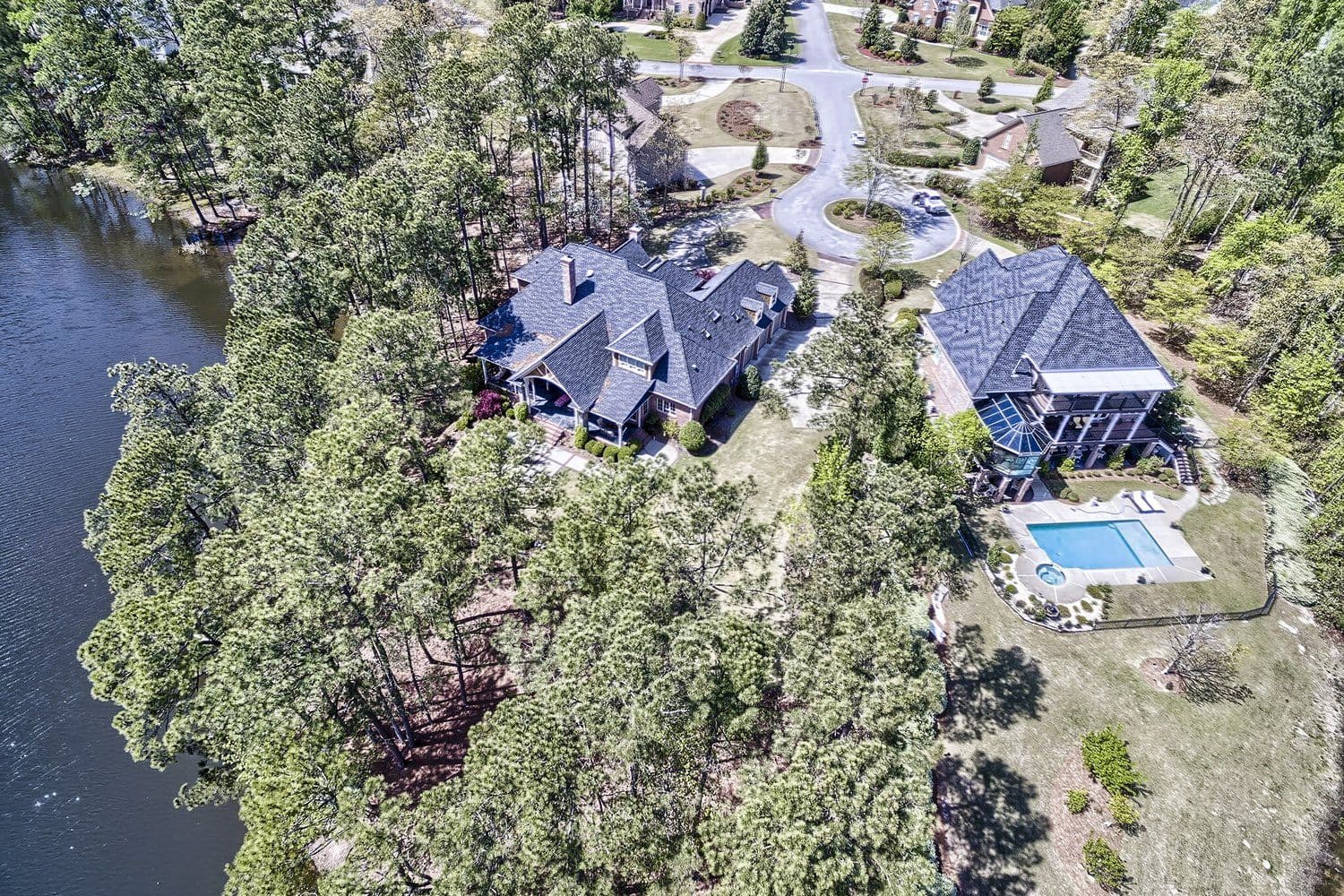 Aerial of a modern dark-shingled house with a backyard pool on a wooded lot