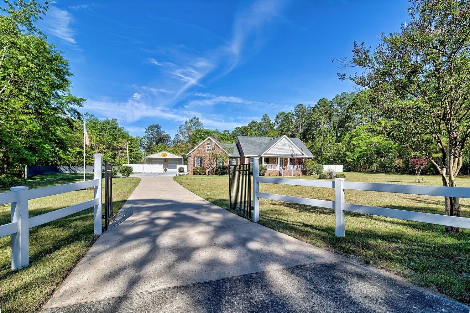 Driveway through a white fence leading to a house among trees