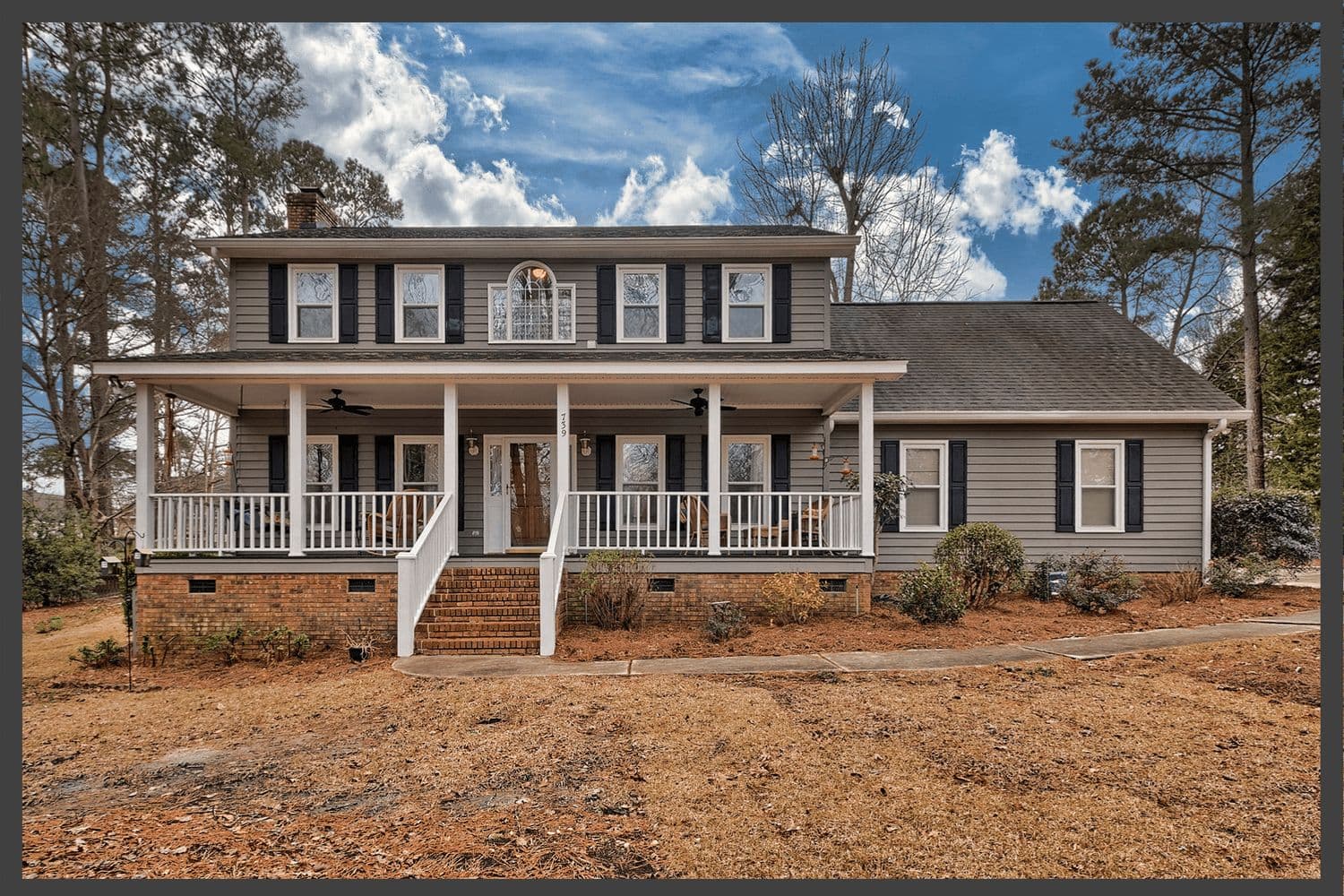 Farmhouse-style home with a full-width porch set against tall pines