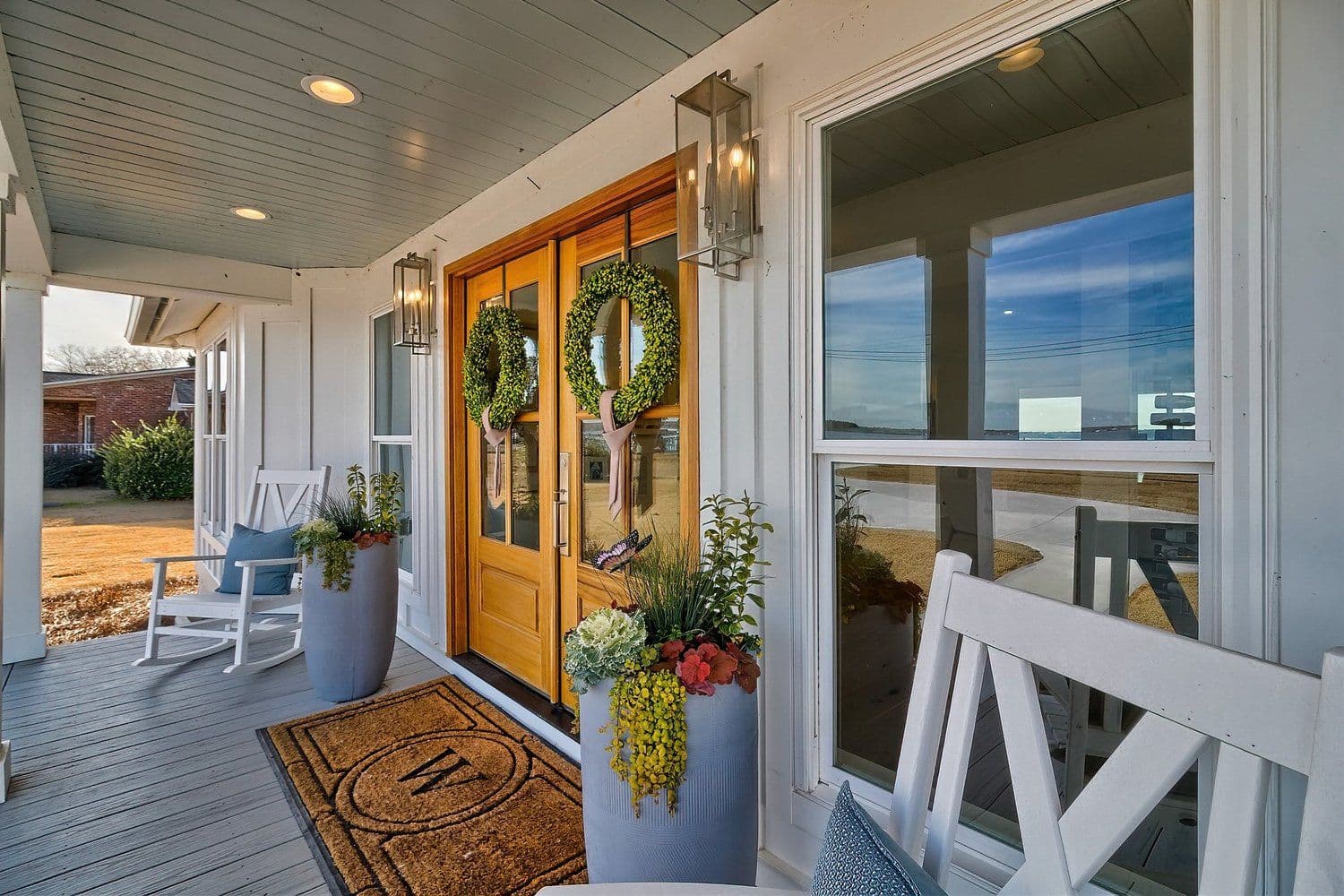 Front porch with a wooden door, wreaths and a white bench