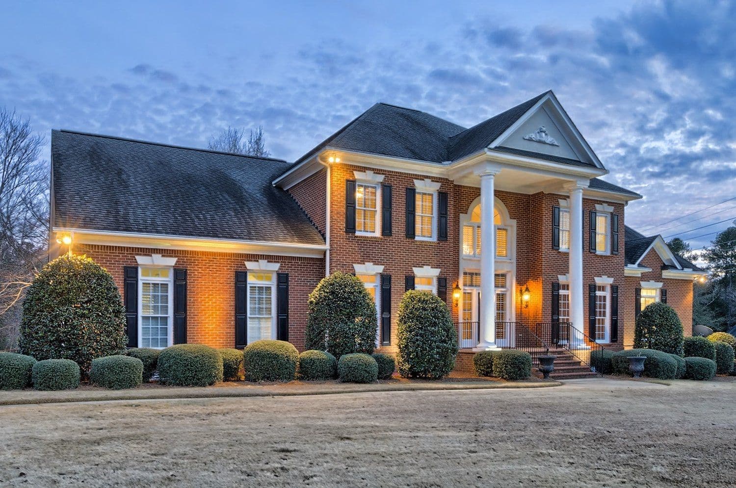 Large brick home at dusk with warm exterior lighting