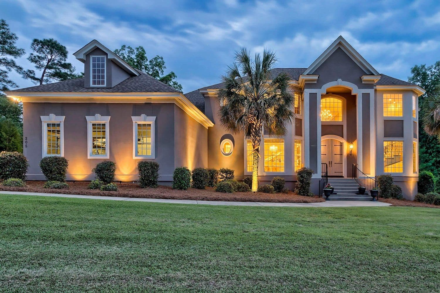 Large home at dusk with warm yellow siding and glowing windows