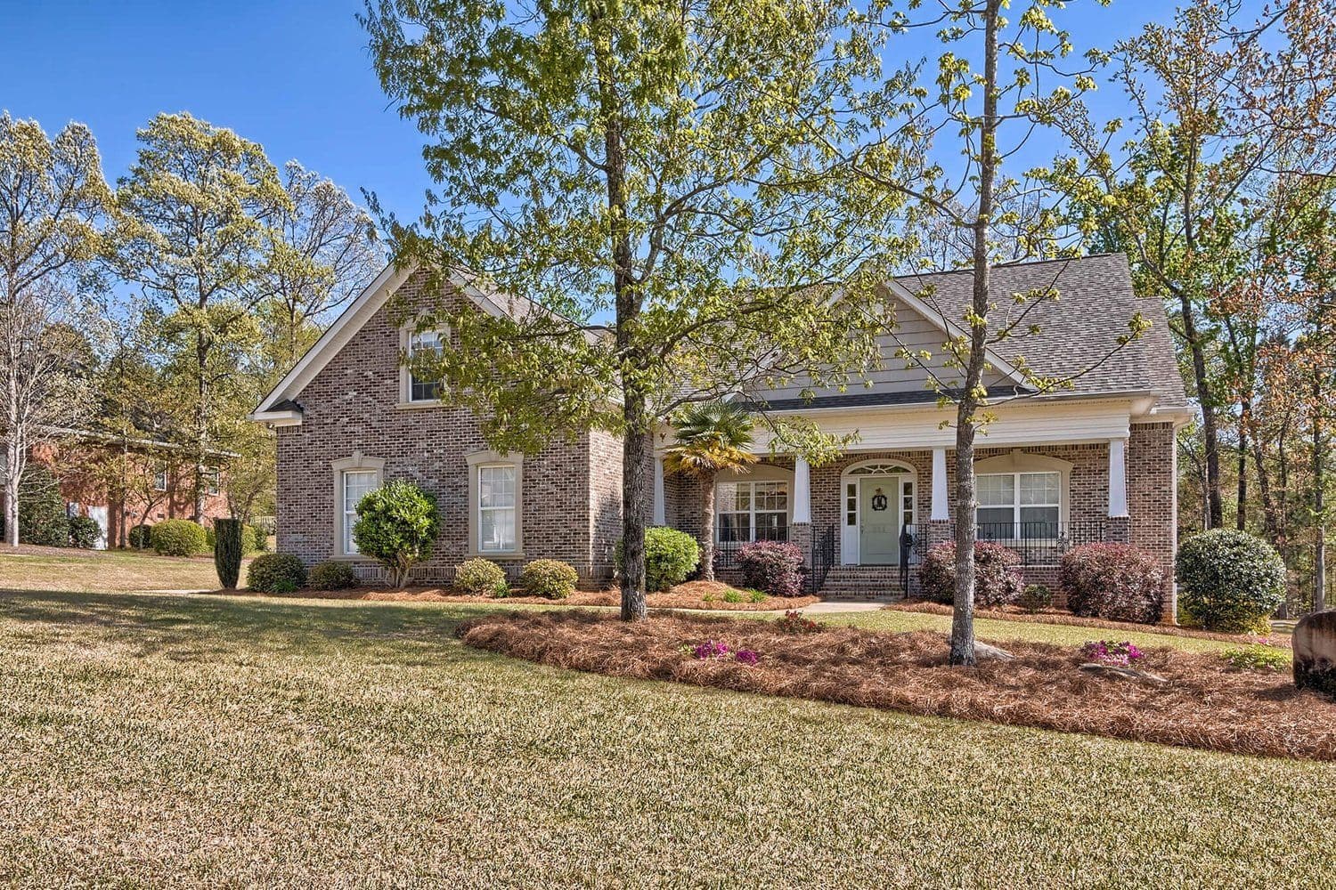 Light brick single-story home with a wide lawn and young trees