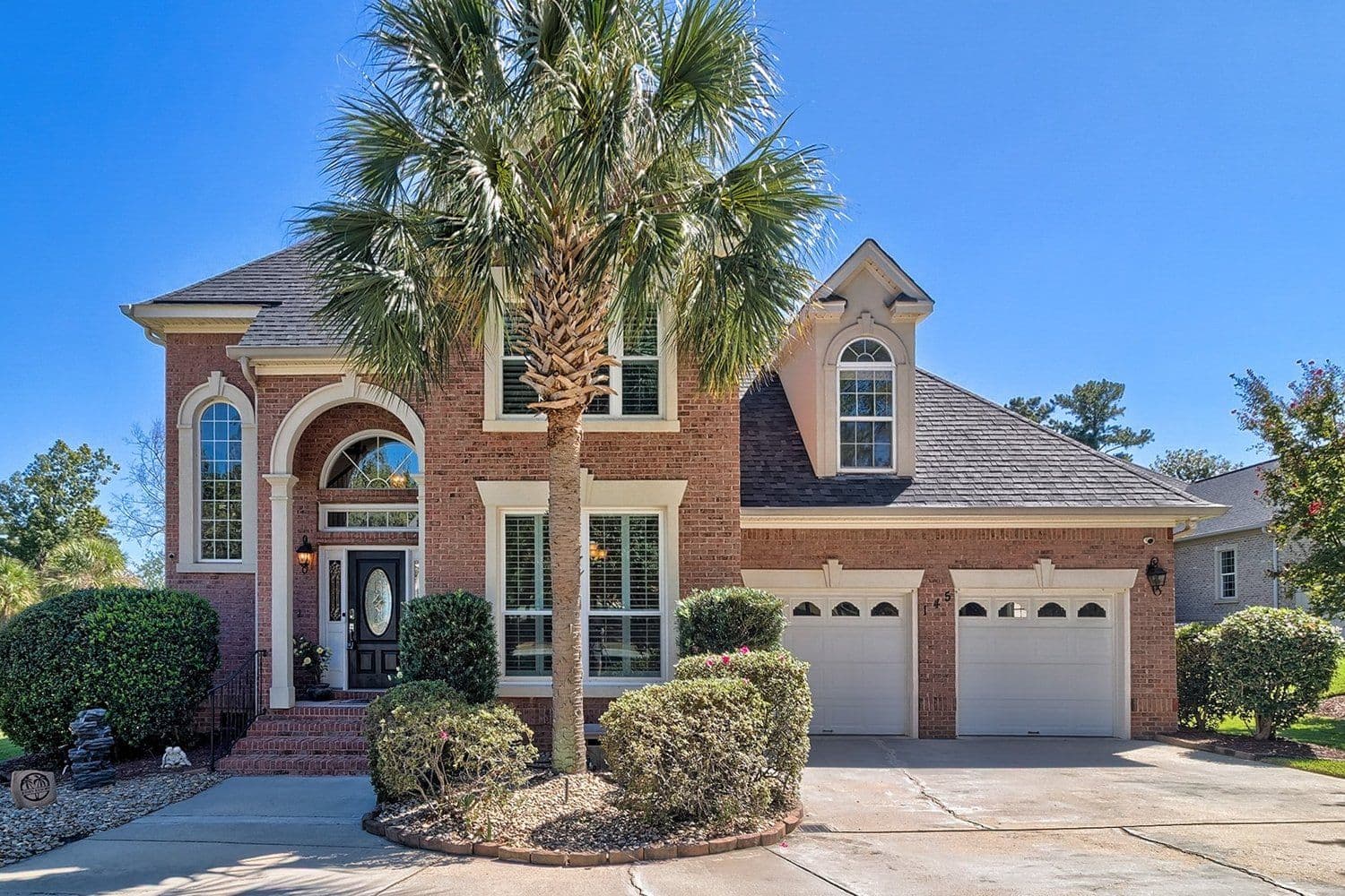 Red brick two-story home with a palm tree in the front yard