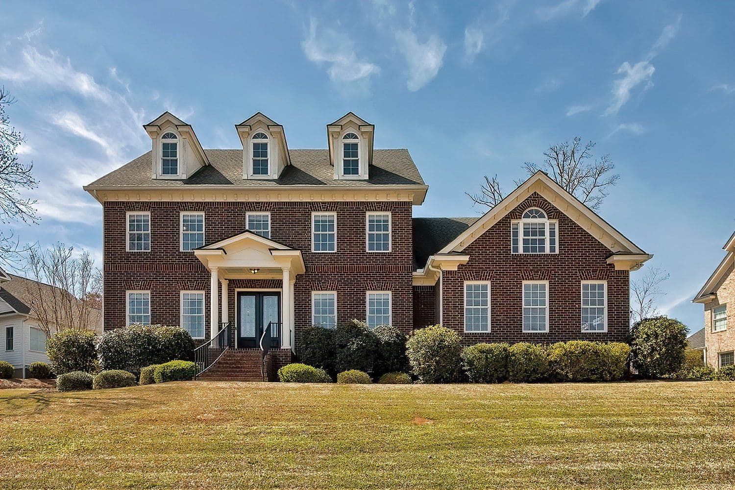 Three-story red brick home with white pillars and a wide lawn