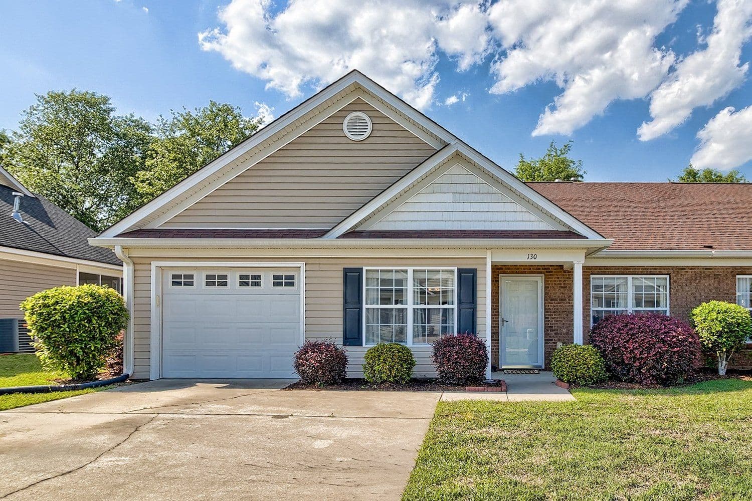 Single-story brick and beige house with a white garage door, dark shutters, and a wide green front lawn
