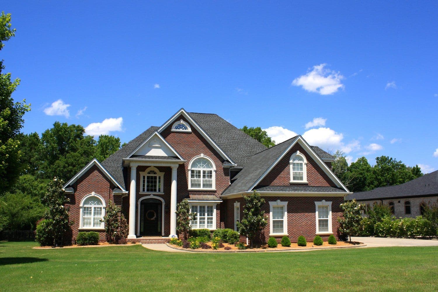 Traditional two-story red brick house with white trim and a wide green lawn