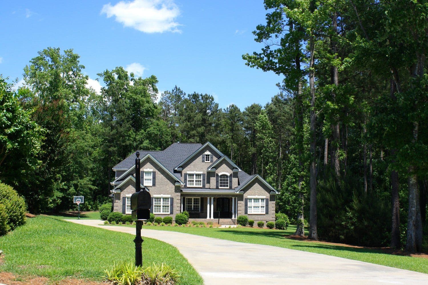 Two-story grey house with white trim in a wooded setting