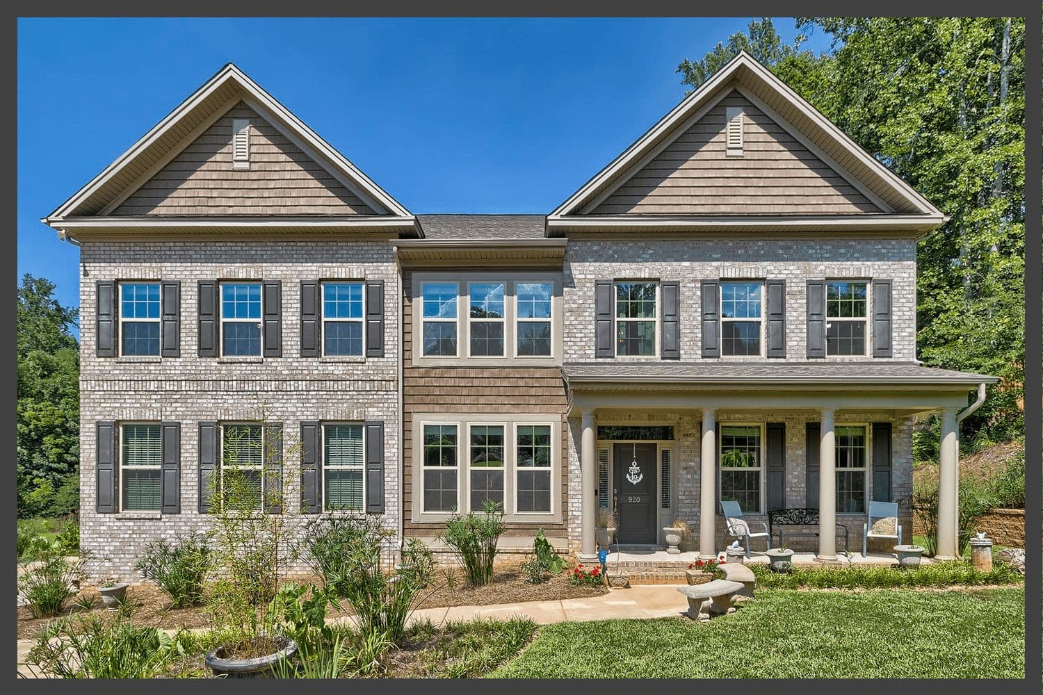 Two-story home with grey siding, stone accents and a large front porch