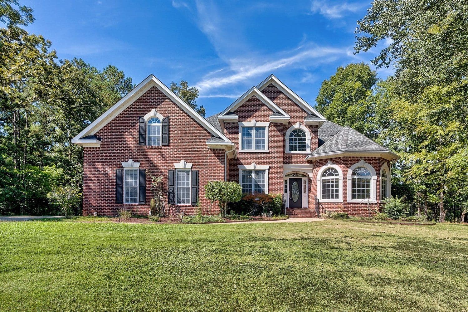 Two-story red brick home with black shutters, a rounded entry, and a wide green lawn