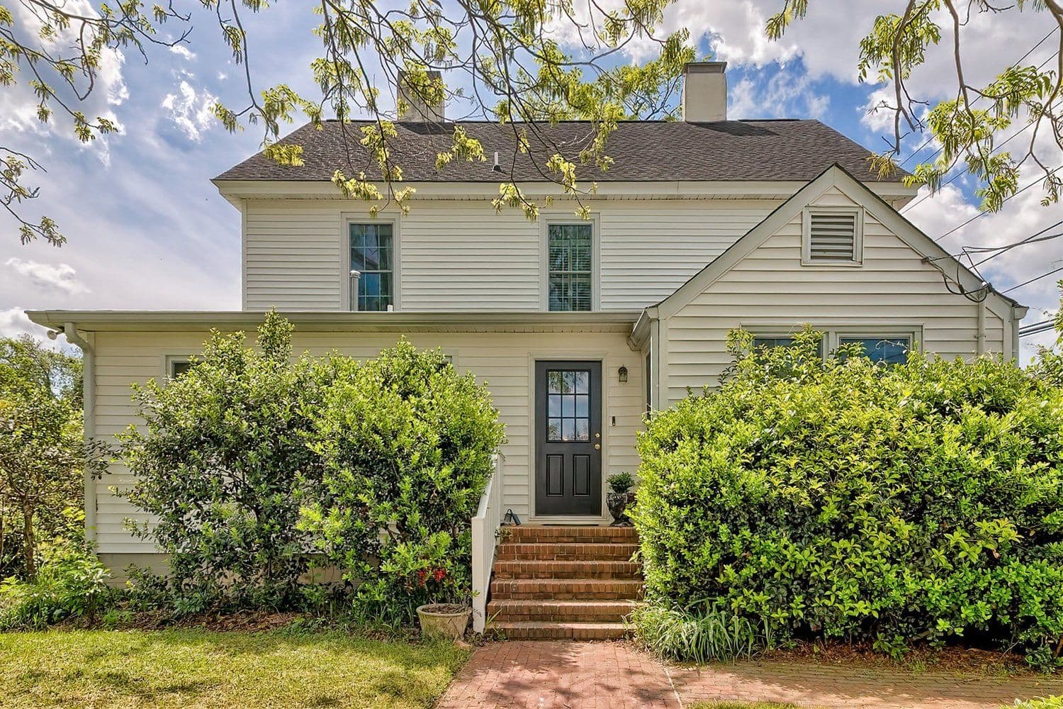White two-story farmhouse-style home with green foundation shrubs