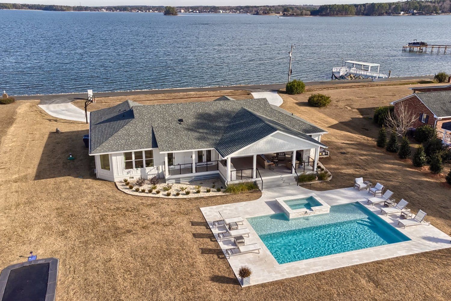 Aerial of a modern white single-story home with a pool and hot tub beside the water
