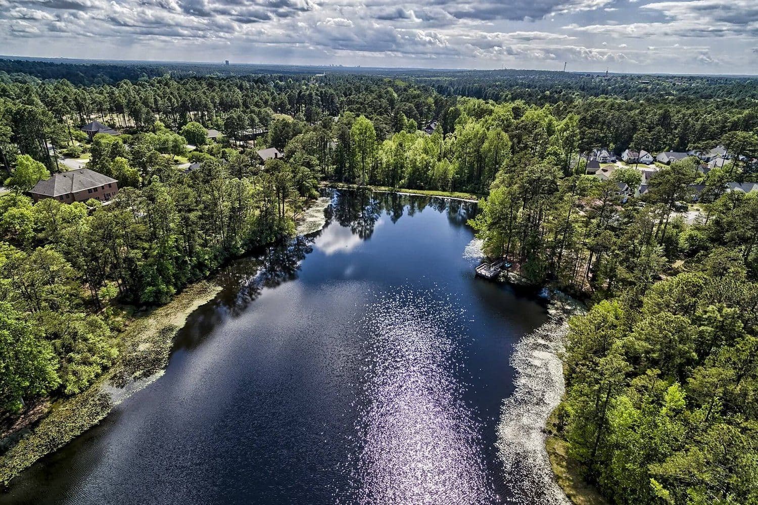 Aerial of a narrow lake inlet winding through a forested residential area
