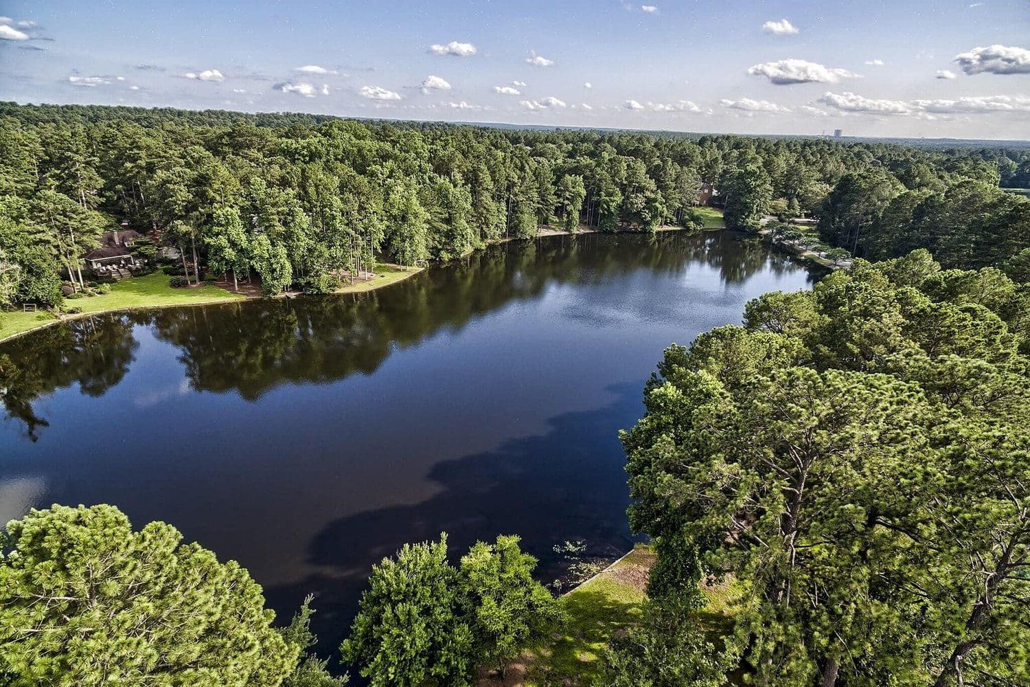 Aerial of a still lake reflecting blue sky inside thick forest