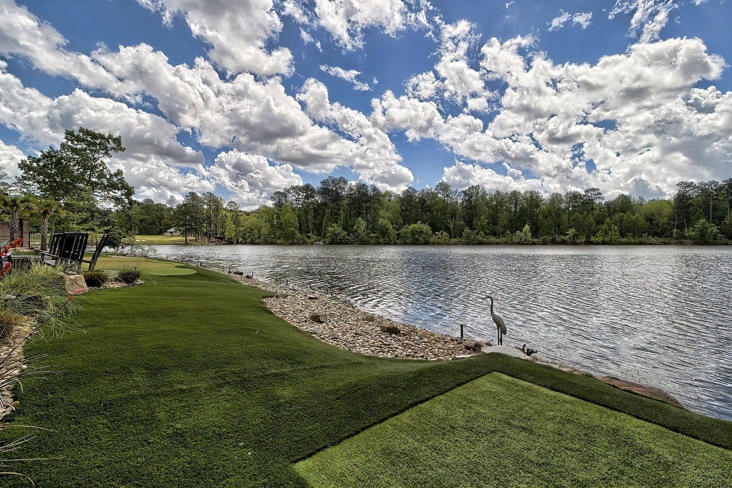 Lake shoreline with a green lawn and fluffy white clouds