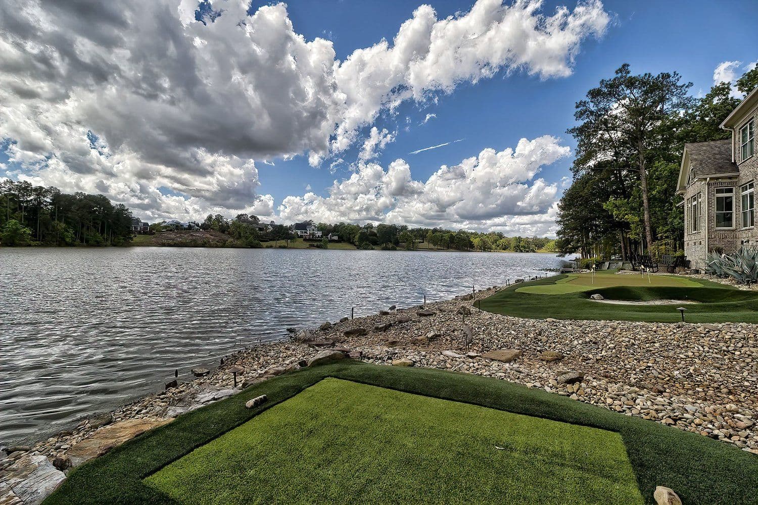 Lake view from a grassy bank with a stone retaining wall under a wide cloudy sky