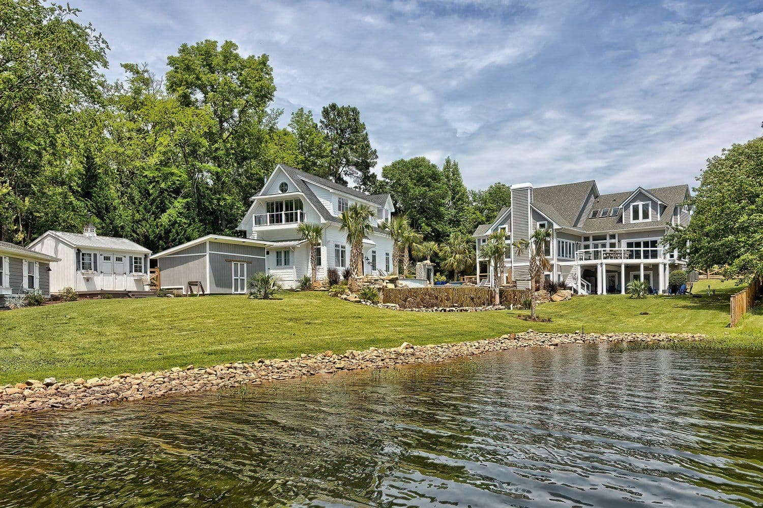 Two large waterfront homes with green lawns reaching the water's edge