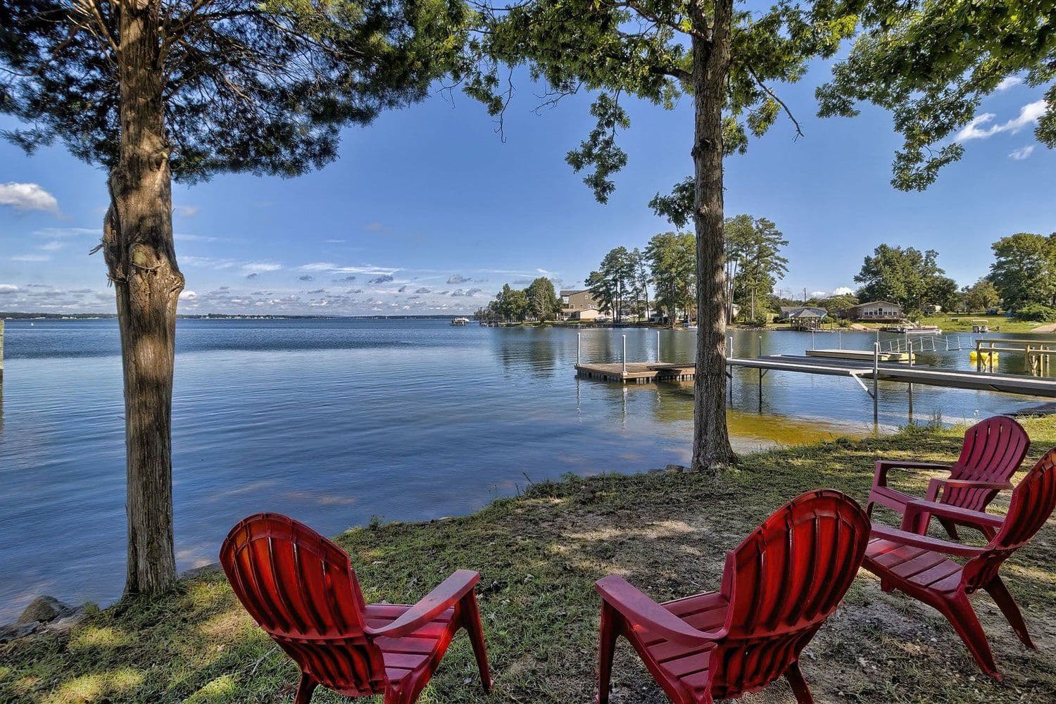 Two red Adirondack chairs on a lawn overlooking the lake