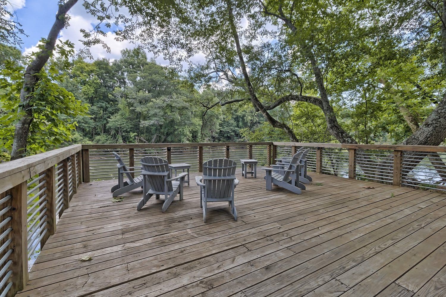Wooden deck with Adirondack chairs arranged in a circle overlooking trees and water