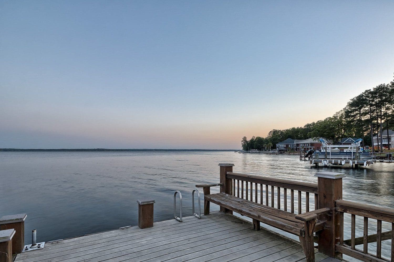 Wooden dock with a bench looking out at a calm lake at dusk