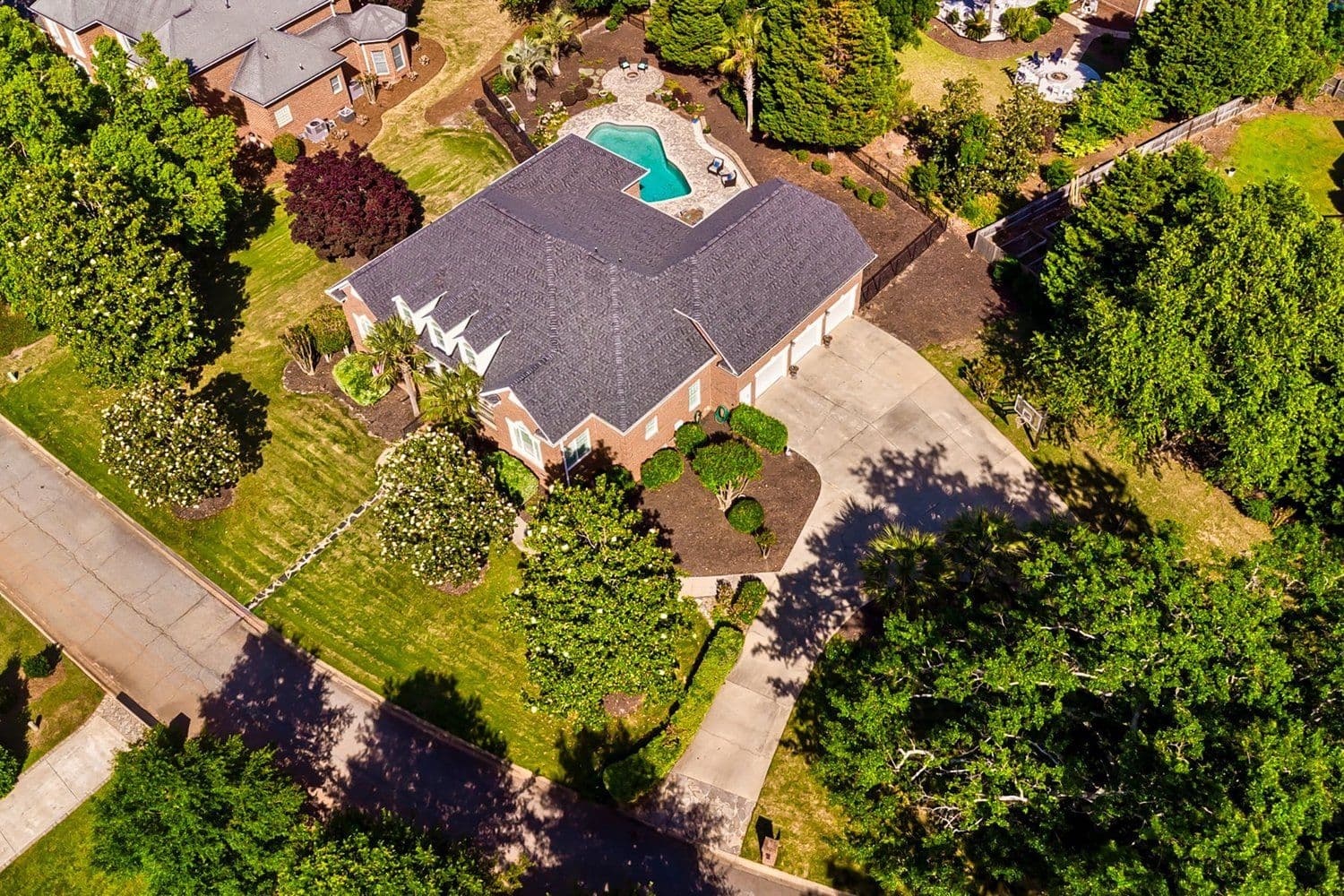 Aerial of a brick house with a backyard pool among green trees