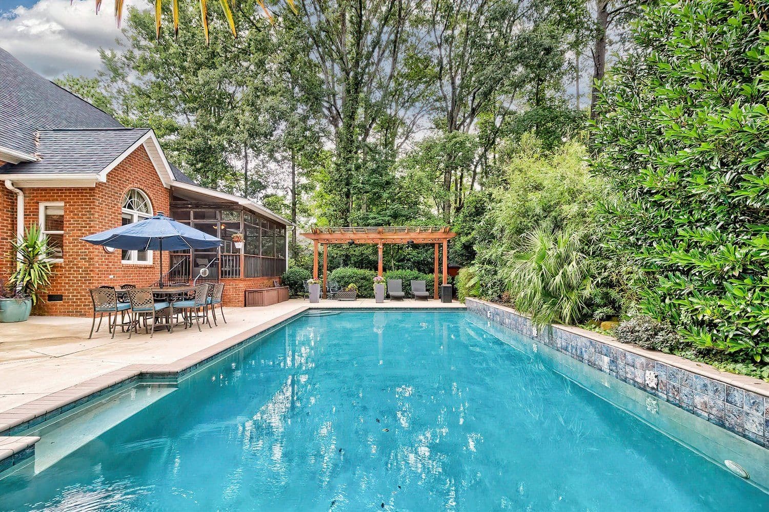 Backyard pool with a stone patio, dining table and wooden pergola