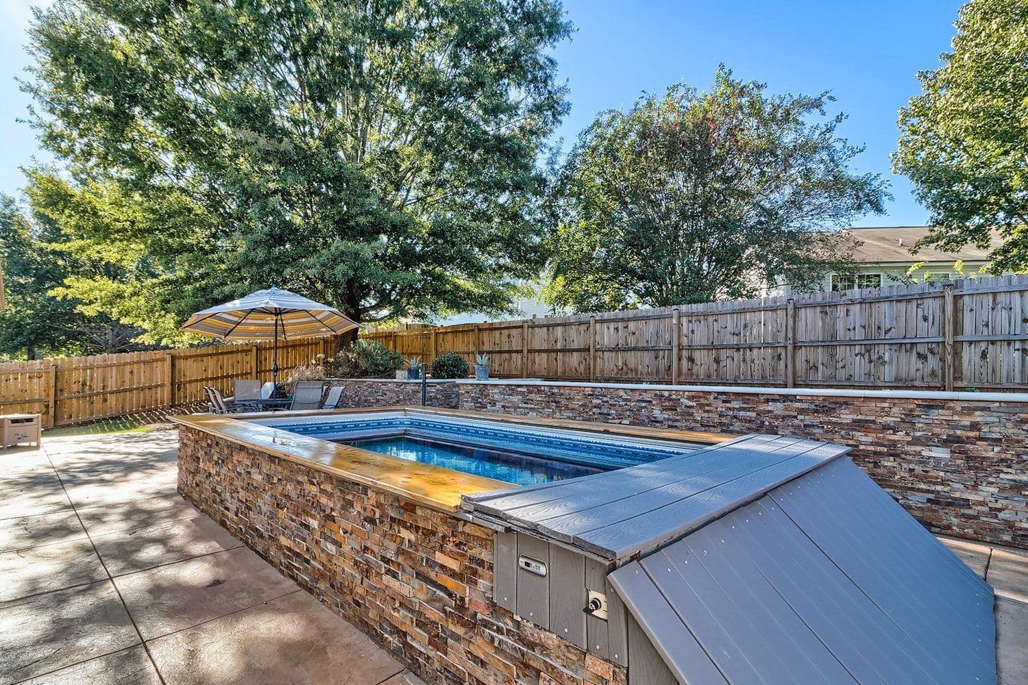 Stone-faced pool area with a wooden fence and green trees
