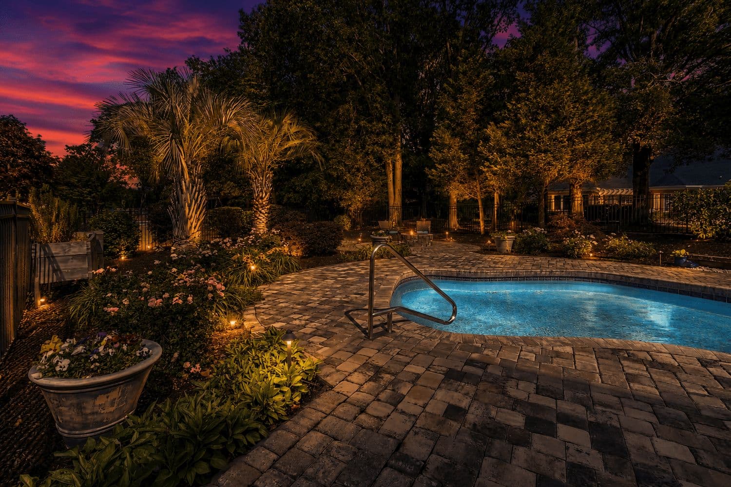 Swimming pool and hot tub lit at night among palm trees