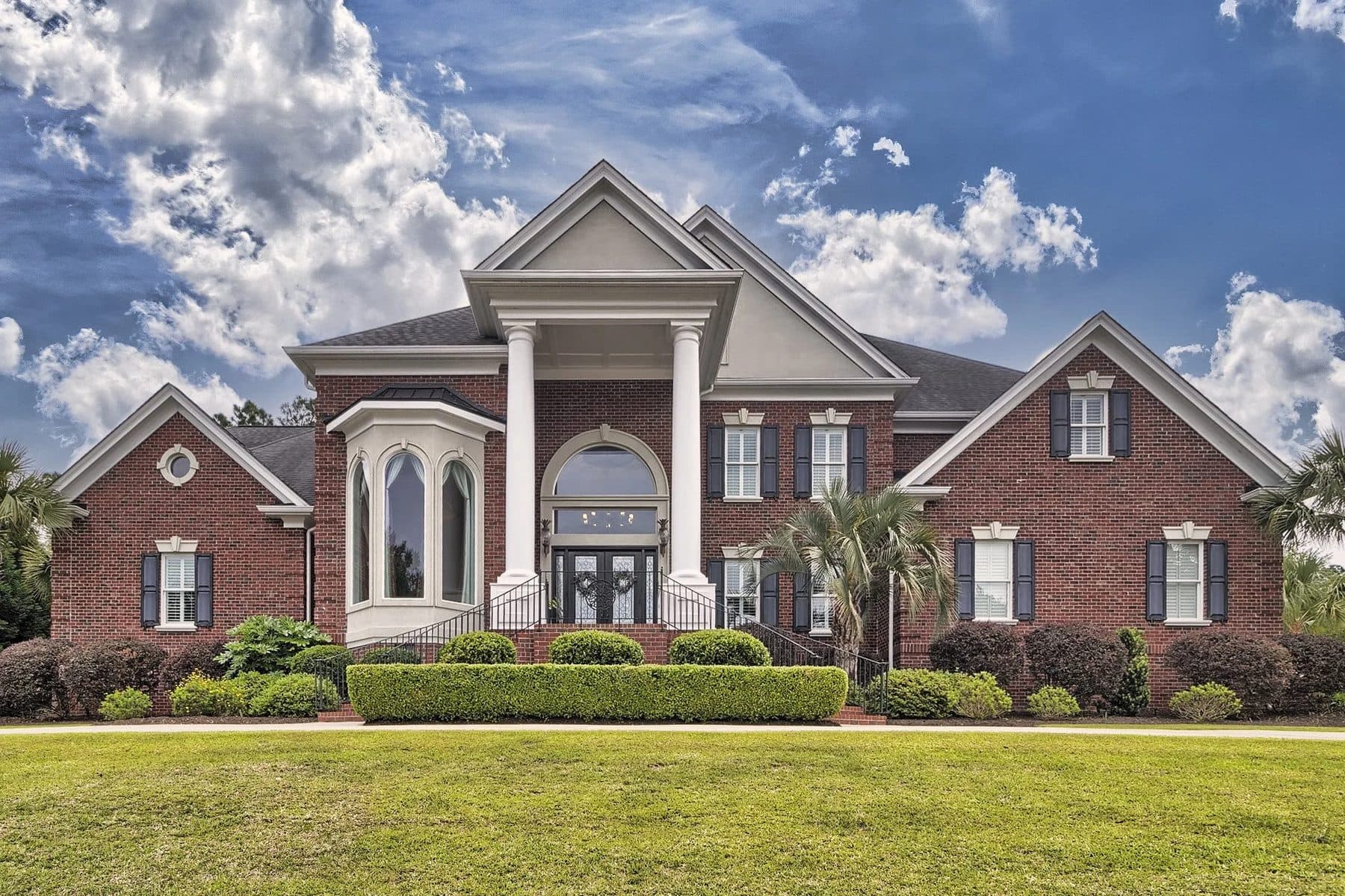 A red brick house with a white portico and palms