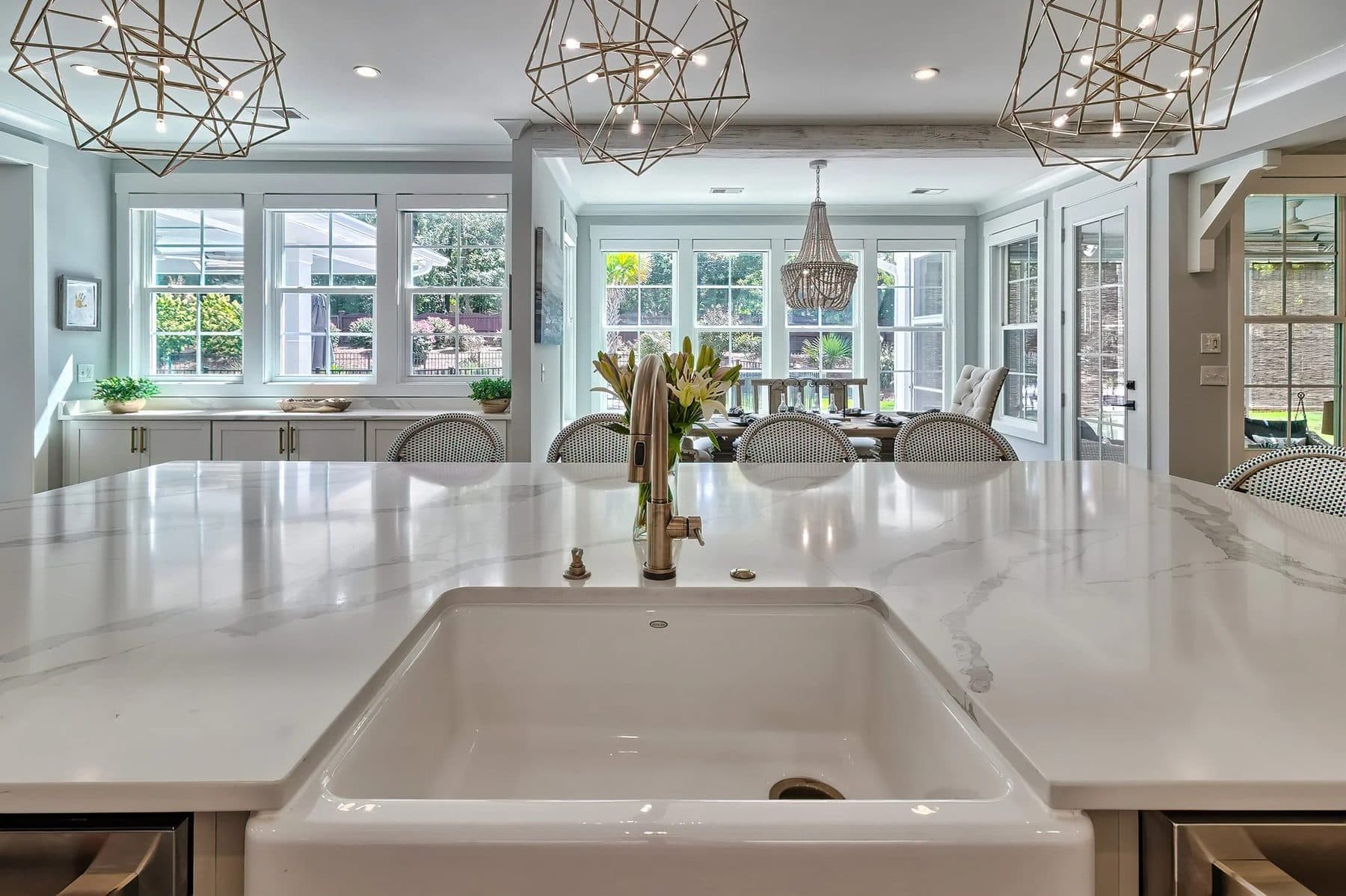 A farmhouse sink facing a dining table and backyard windows