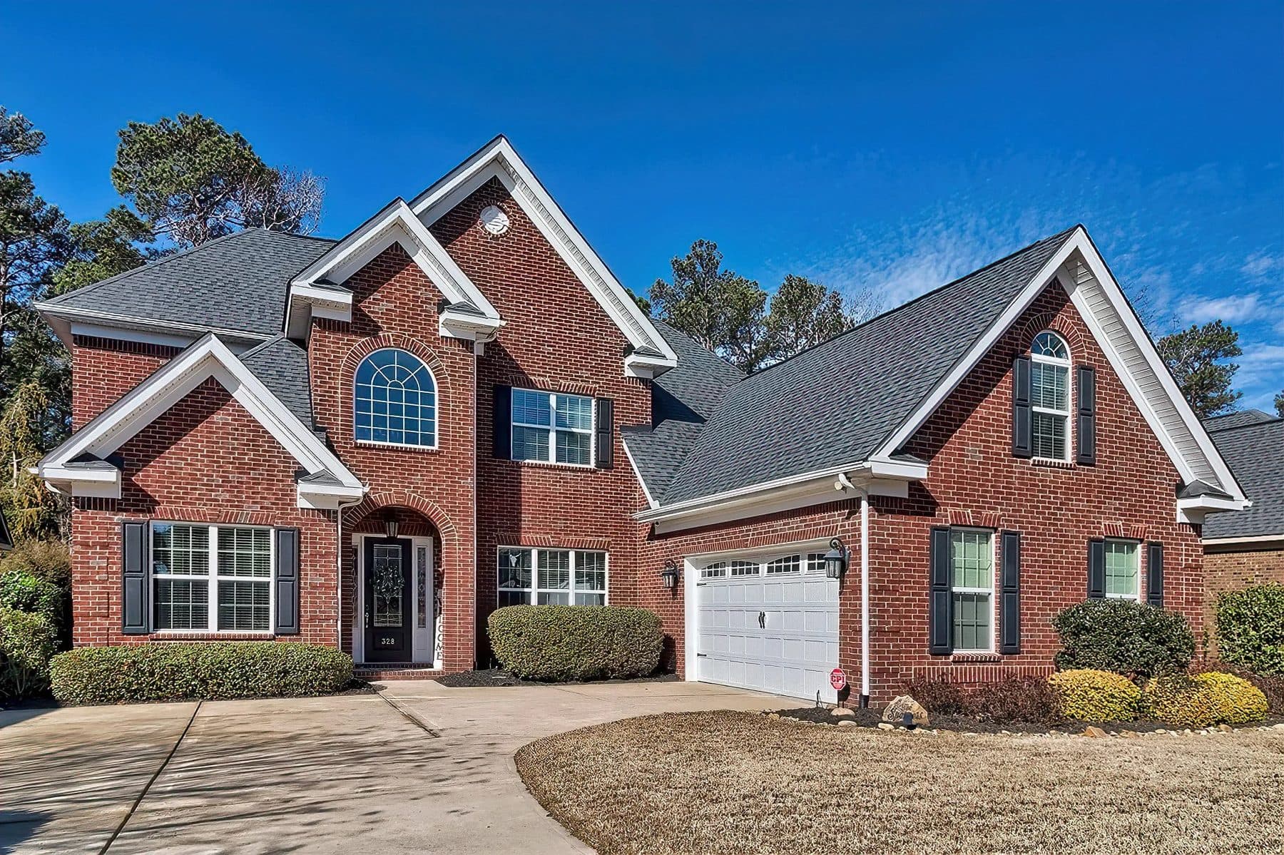 A brick house with white trim, a front walk, and a green lawn