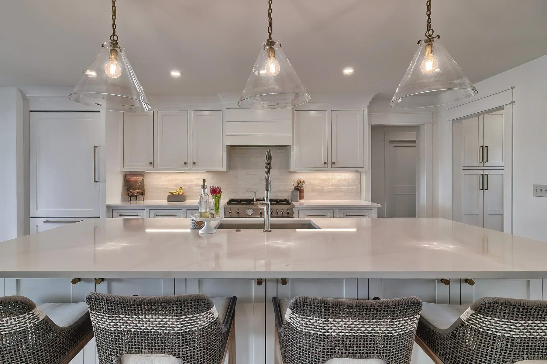 A white kitchen with an island and glass pendant lights